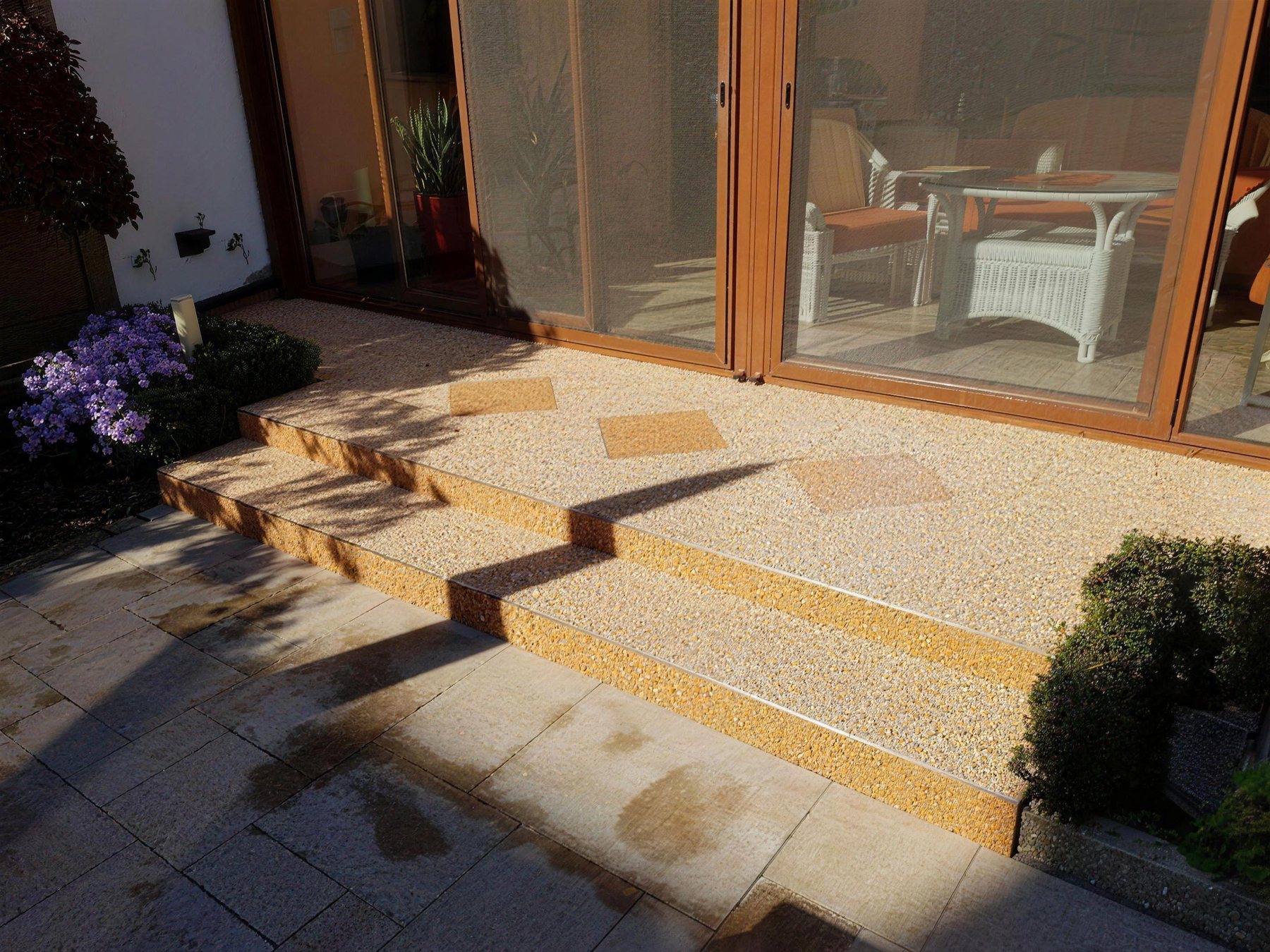 Terrasse mit Stufen vor einer Glasfront, Belag in warmer Körnung mit Einlegemuster