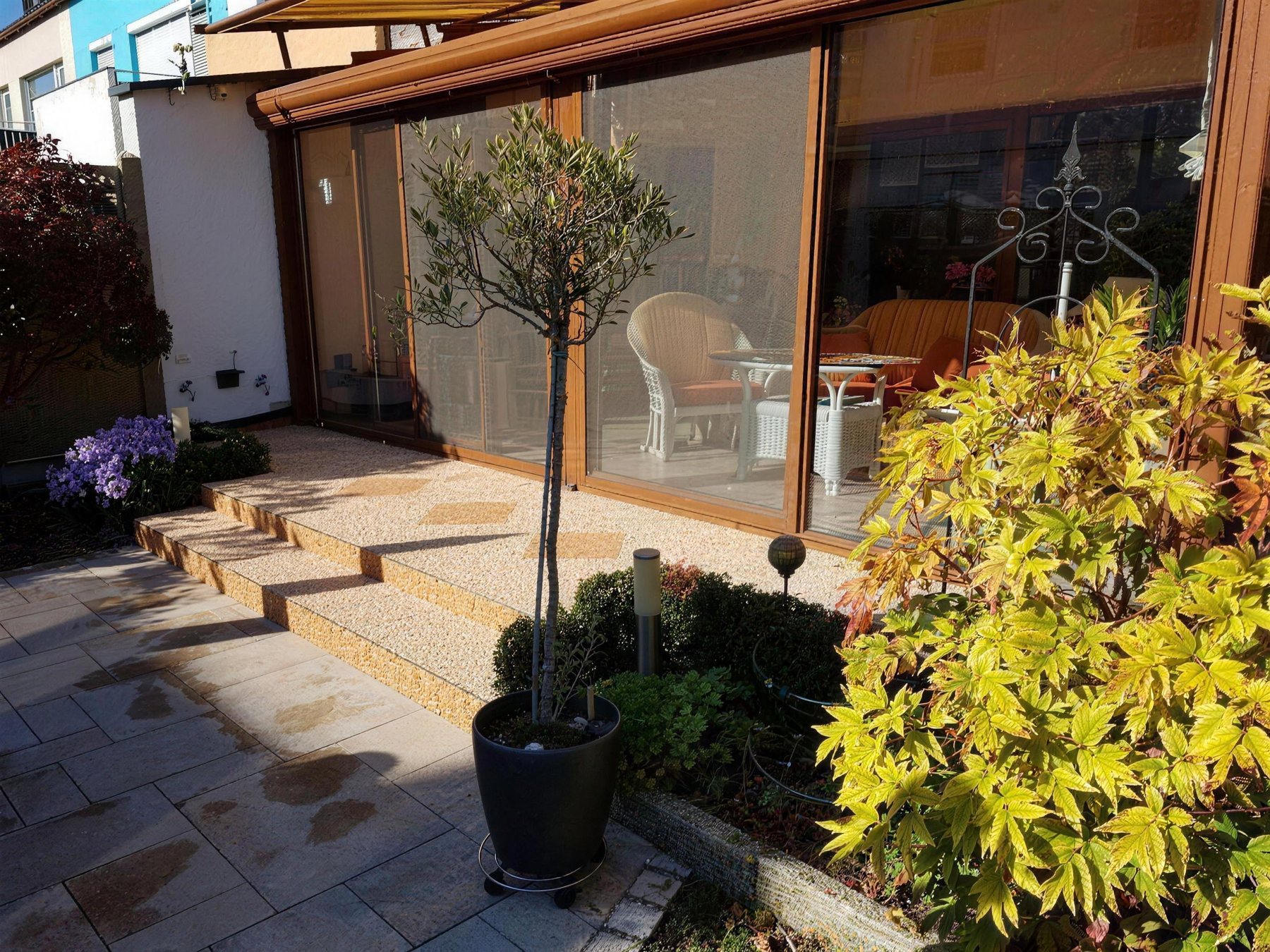 Sonnige Terrasse mit neuem Belag, Stufen und Pflanzkübeln vor einem Wintergarten